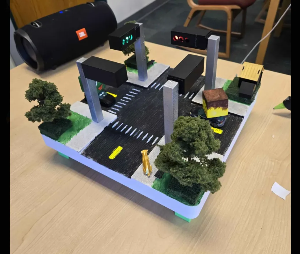 Scale model of a four-way intersection with lit traffic signals, painted crosswalks, and model trees
